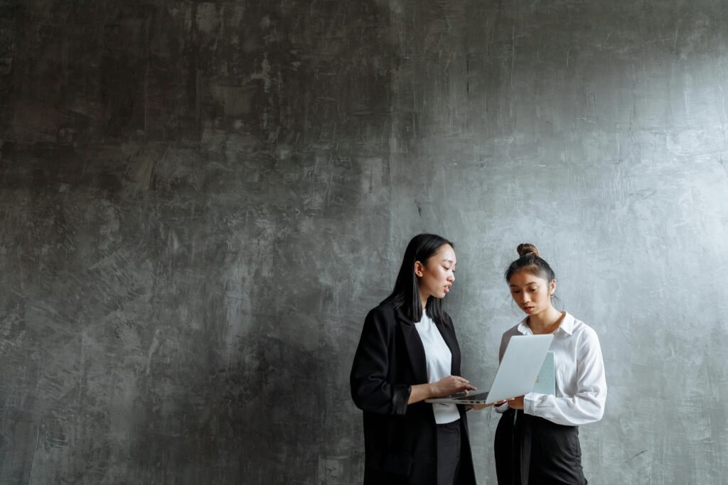Two professional women collaborating with a laptop in a modern office setting.