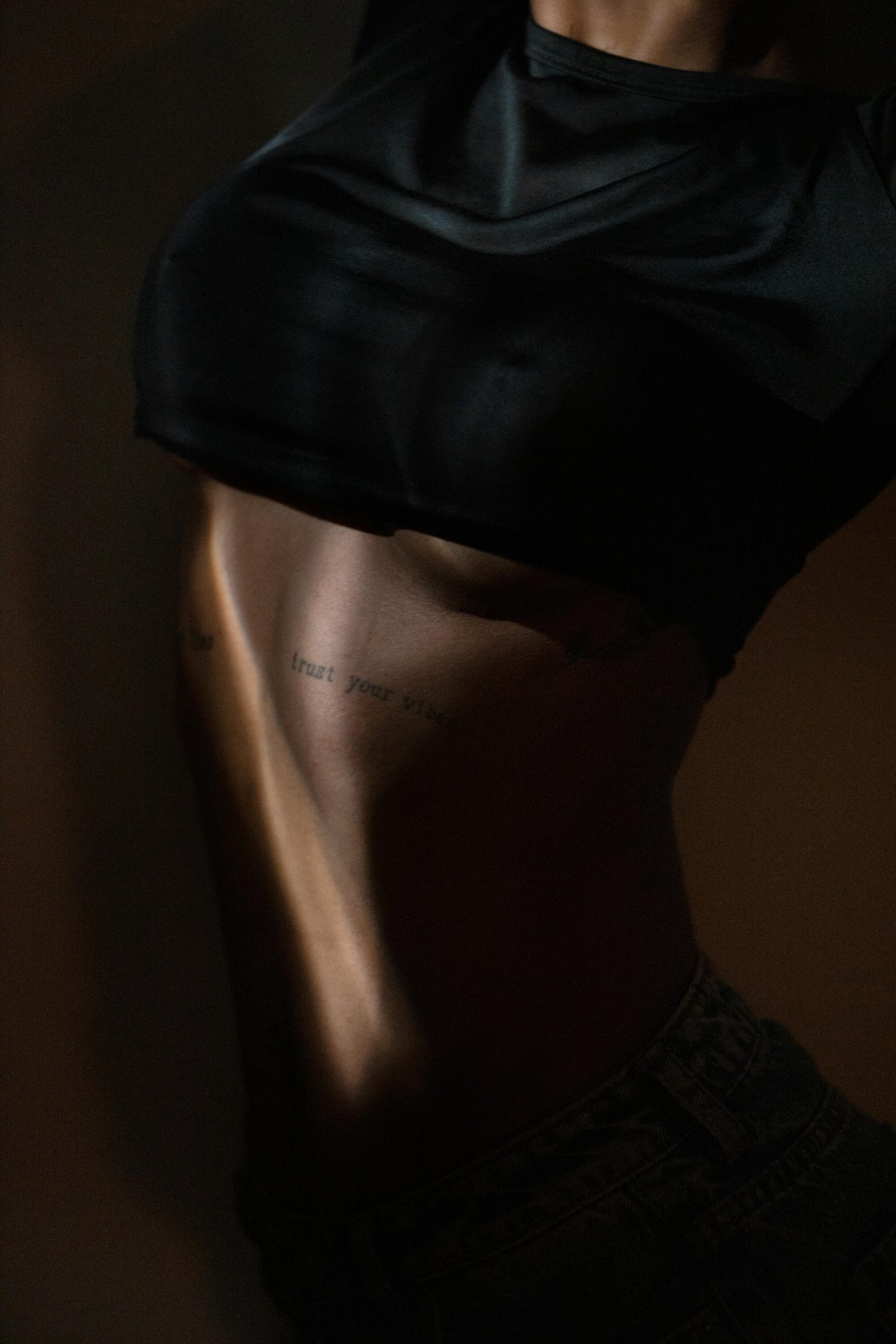 A dramatic and artistic close-up of a tattooed abdomen, capturing the interplay of light and shadow on skin.
