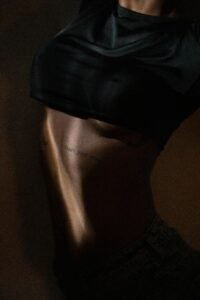 A dramatic and artistic close-up of a tattooed abdomen, capturing the interplay of light and shadow on skin.